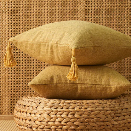 Housse de coussin jaune avec pompons, posée sur un tapis en osier, apportant une touche déco chaleureuse