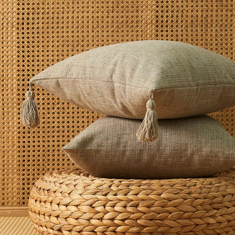 Coussins décoratifs beiges avec pompons, posés sur un pouf en osier dans un intérieur chaleureux