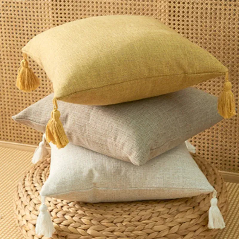 Coussins décoratifs empilés avec pompons, en teintes jaune, beige et blanc, sur un tapis en jute