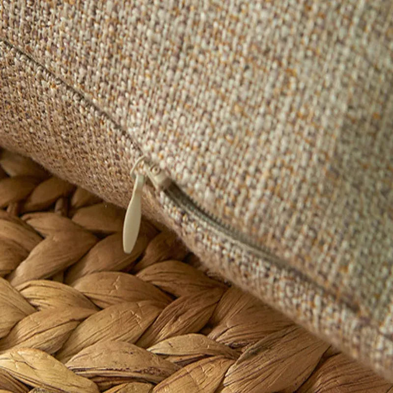 Housse de coussin beige texturé avec fermeture éclair, posée sur un tapis en jute tressé