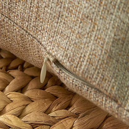 Housse de coussin beige texturé avec fermeture éclair, posée sur un tapis en jute tressé