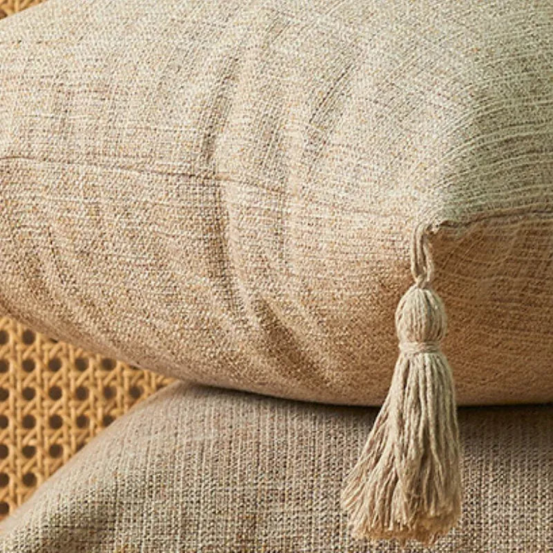 Housse de coussin beige texturé avec pompon, décorant un canapé dans un salon moderne