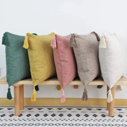 Coussins décoratifs aux teintes variées avec pompons, disposés sur un banc en bois sur un tapis moderne