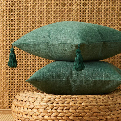 Deux coussins décoratifs verts en lin avec pompons, posés sur un tapis en jute dans un intérieur chaleureux