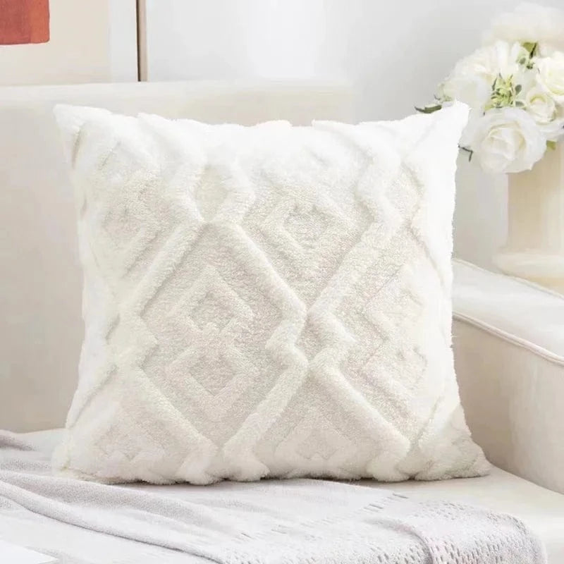 Coussin décoratif blanc en velours avec motifs géométriques, posé sur un canapé élégant dans un salon lumineux