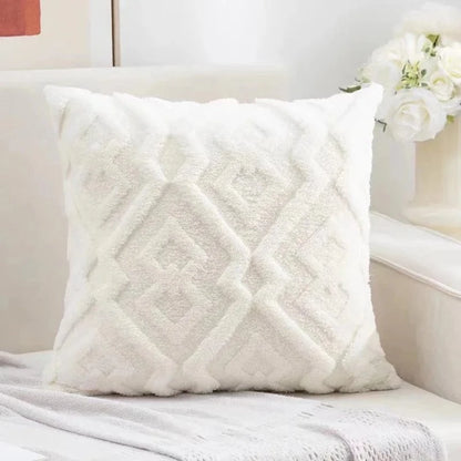 Coussin décoratif blanc en velours avec motifs géométriques, posé sur un canapé élégant dans un salon lumineux