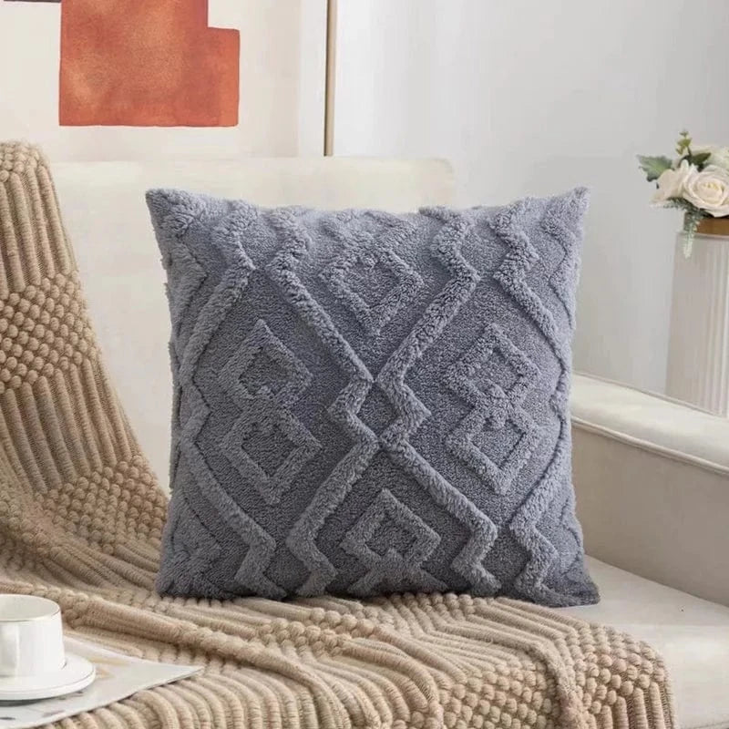 Coussin décoratif gris en velours avec motifs géométriques, posé sur un canapé beige dans un salon moderne