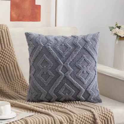 Coussin décoratif gris en velours avec motifs géométriques, posé sur un canapé beige dans un salon moderne