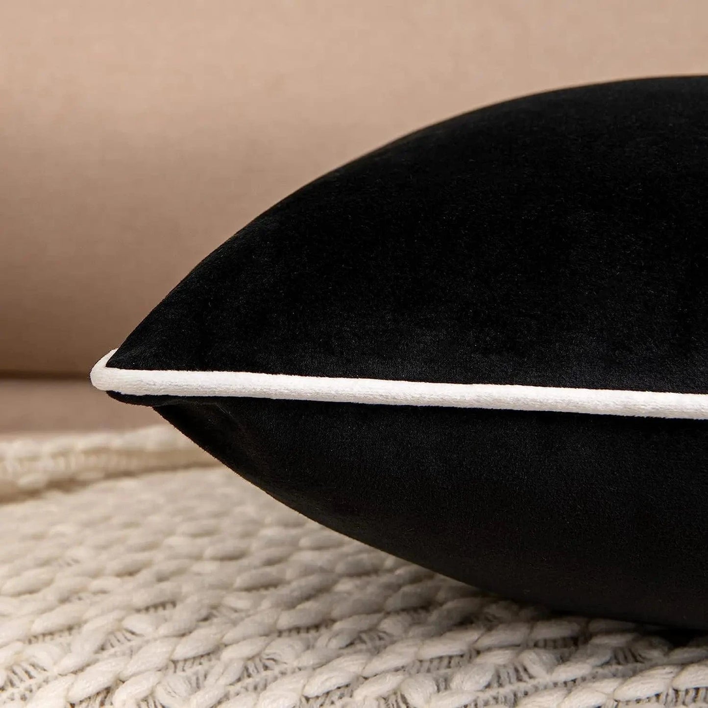 Coussin décoratif noir en velours avec une bordure blanche, posé sur un tapis en laine dans un salon moderne