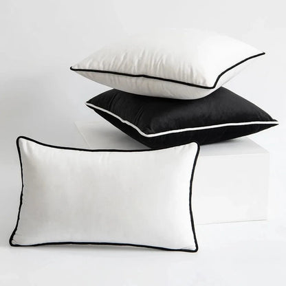 Trois coussins décoratifs, un noir et deux blancs, avec des bordures contrastantes, sur une surface blanche
