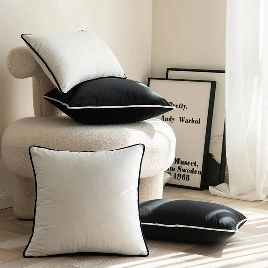 Coussins décoratifs noir et blanc avec bordure, posés sur un fauteuil dans un salon lumineux et moderne
