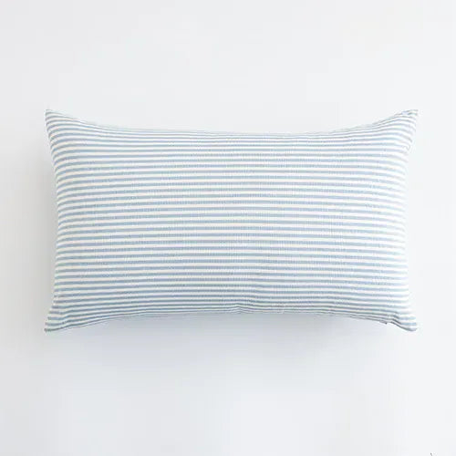 Housse de coussin bleu ciel à rayures blanches, posée sur un canapé moderne et élégant