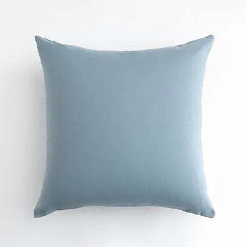 Housse de coussin bleu ciel, simple et élégante, posée sur un canapé moderne dans un salon lumineux