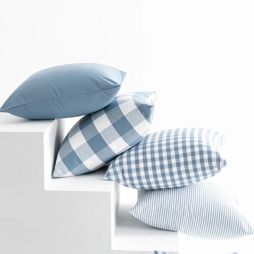 Housses de coussin bleu ciel avec motifs à carreaux et rayures, disposées sur des marches blanches