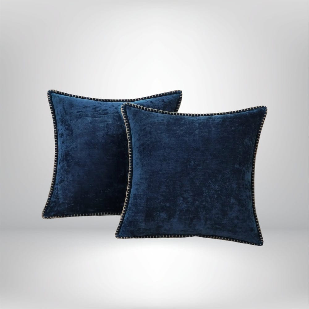 Deux coussins décoratifs en velours bleu, avec un bord contrasté, posés sur un fond neutre