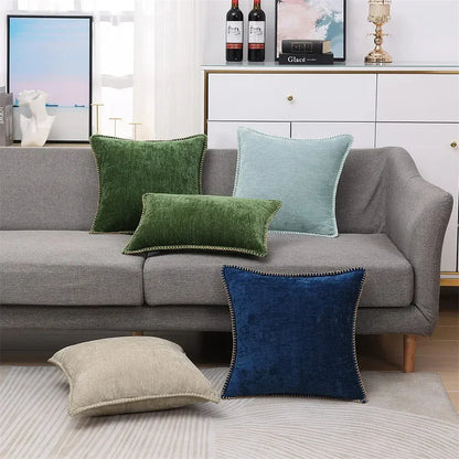 Coussins décoratifs de différentes couleurs sur un canapé gris, incluant des textures douces et des bordures contrastantes