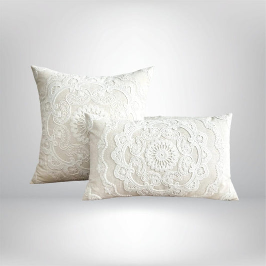 Housse de coussin décorative brodée en blanc, posée sur un fond neutre, avec des motifs floraux élégants
