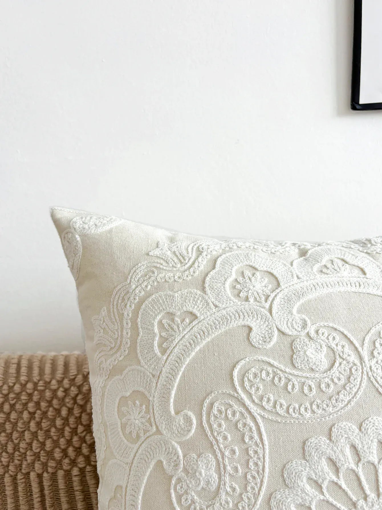 Housse de coussin brodée en beige avec motifs floraux, posée sur un canapé texturé