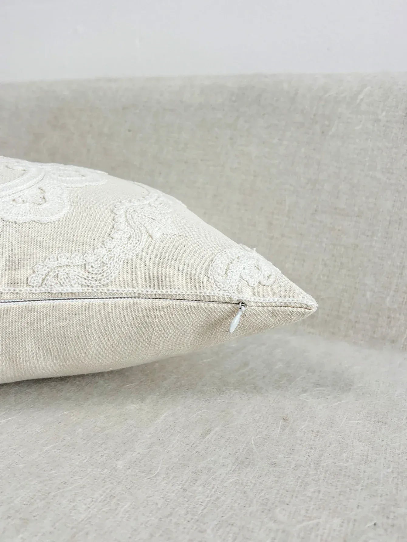 Housse de coussin brodée beige sur un canapé, avec un motif délicat et une finition élégante