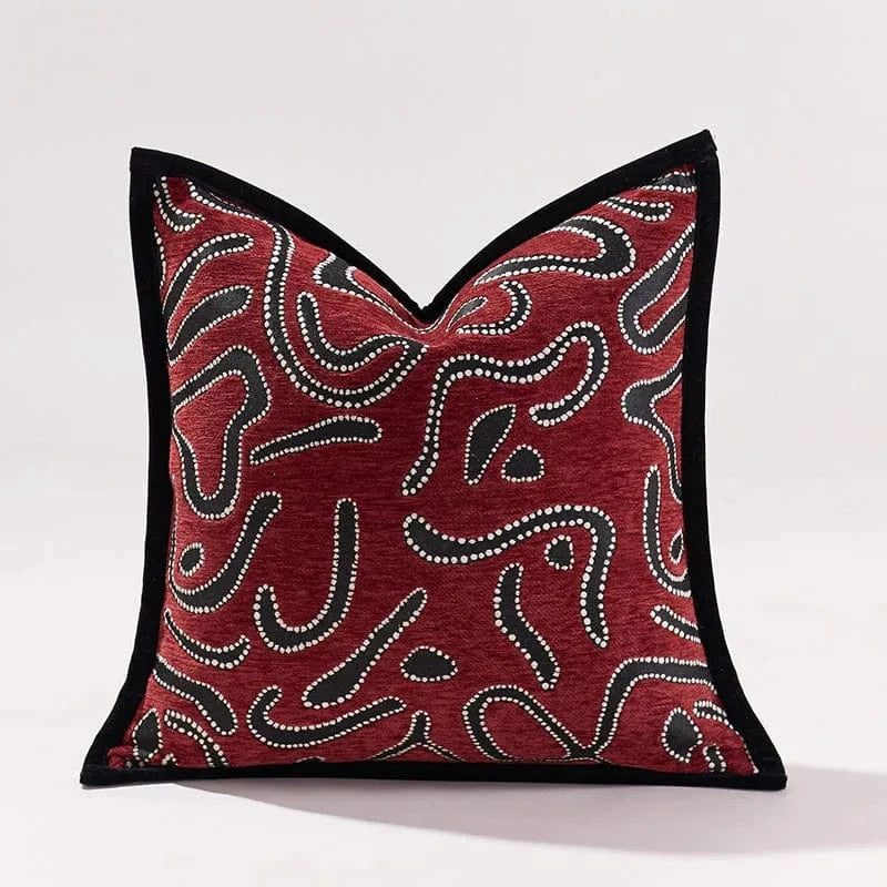 Coussin décoratif rouge avec motifs abstraits noirs et blancs, posé sur un canapé moderne dans un salon élégant