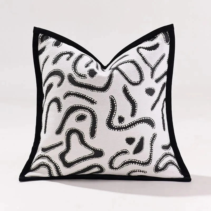 Coussin décoratif en tissu blanc avec motifs abstraits noirs, posé sur un canapé moderne dans un intérieur raffiné