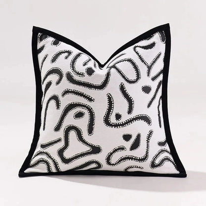 Coussin décoratif en tissu blanc avec motifs abstraits noirs, posé sur un canapé moderne dans un intérieur raffiné