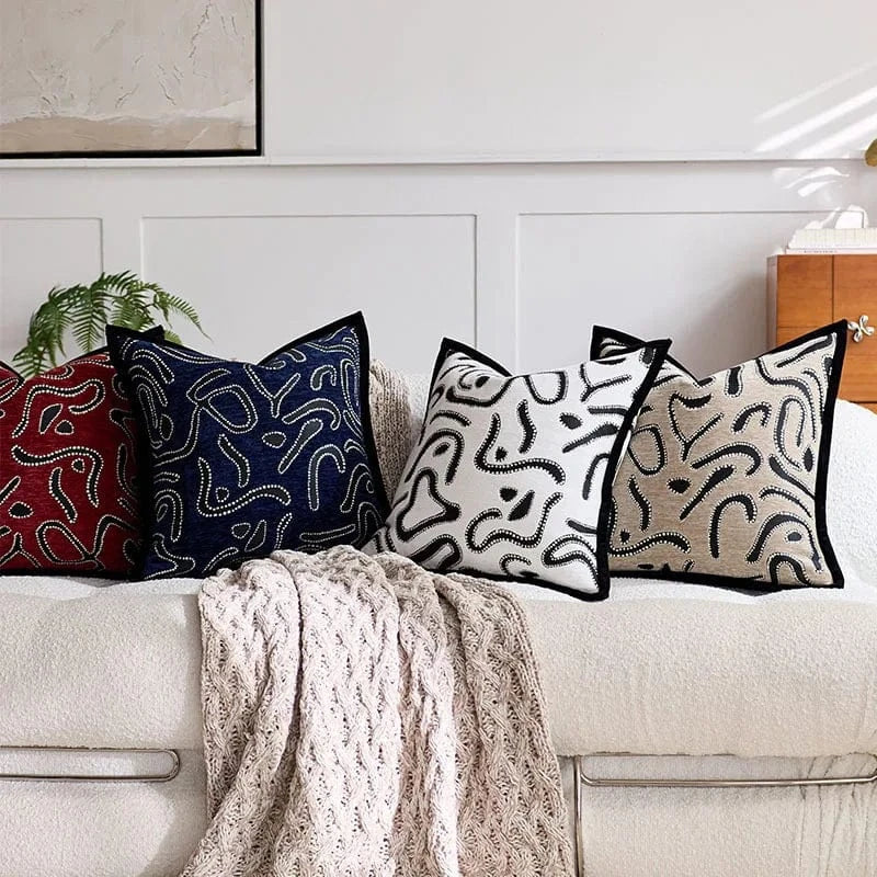 Coussins décoratifs aux motifs abstraits en noir, blanc et rouge, disposés sur un canapé moderne avec un plaid