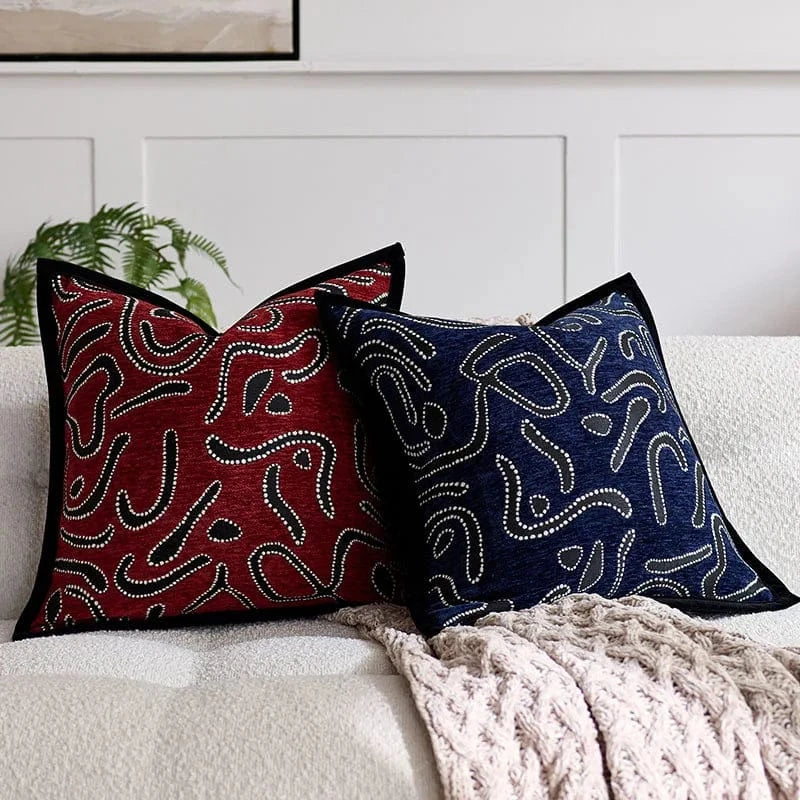 Deux coussins décoratifs en tissu rouge et bleu avec motifs abstraits, posés sur un canapé moderne