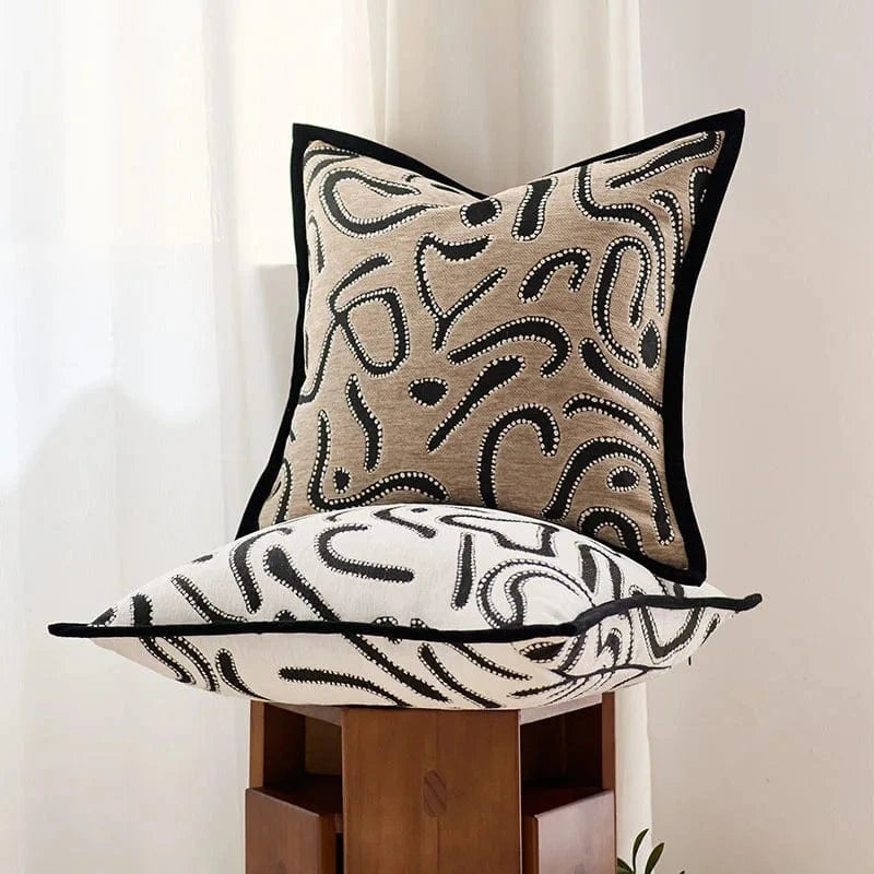 Coussins décoratifs en tissu beige et blanc avec motifs abstraits, posés sur une chaise en bois dans un salon moderne