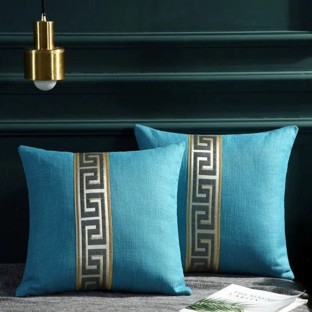Coussins décoratifs turquoise avec motif géométrique noir et doré, posés sur un canapé gris