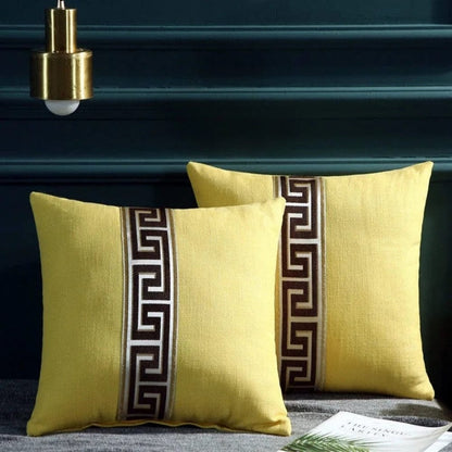 Deux coussins décoratifs jaunes avec un motif géométrique marron, posés sur un canapé gris dans un salon