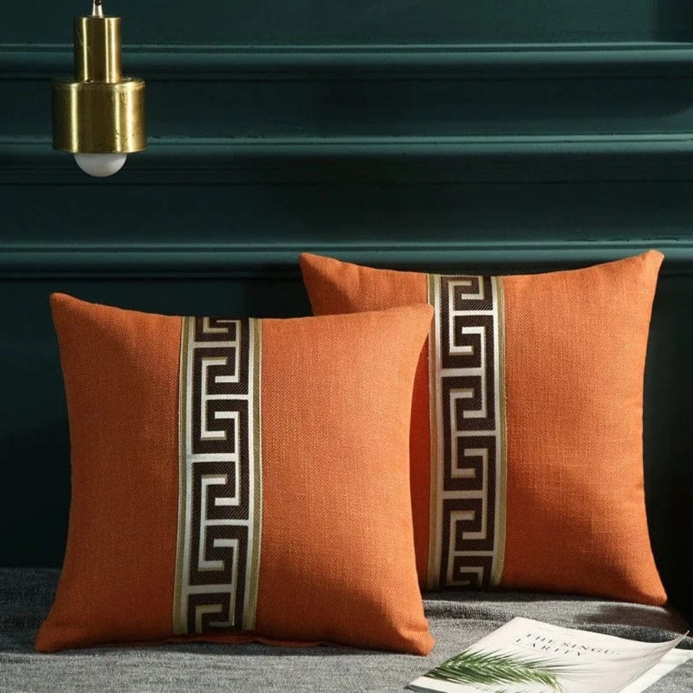 Deux coussins décoratifs orange avec un motif géométrique noir et beige, posés sur un canapé gris