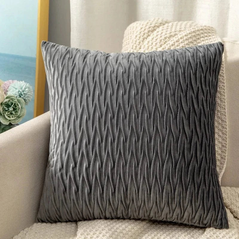 Coussin déco en velours gris avec un motif texturé, posé sur un canapé beige dans un salon moderne