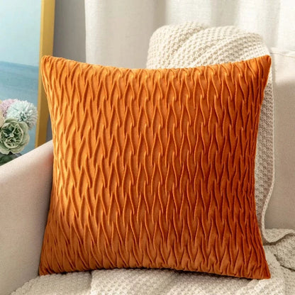 Coussin décoratif en velours orange avec un motif texturé, posé sur un canapé beige dans un salon moderne