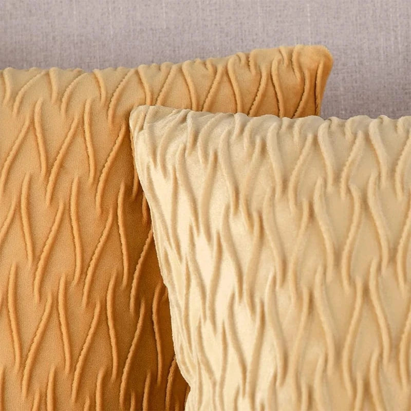 Deux coussins décoratifs en velours beige avec un motif ondulé, posés sur un fond neutre