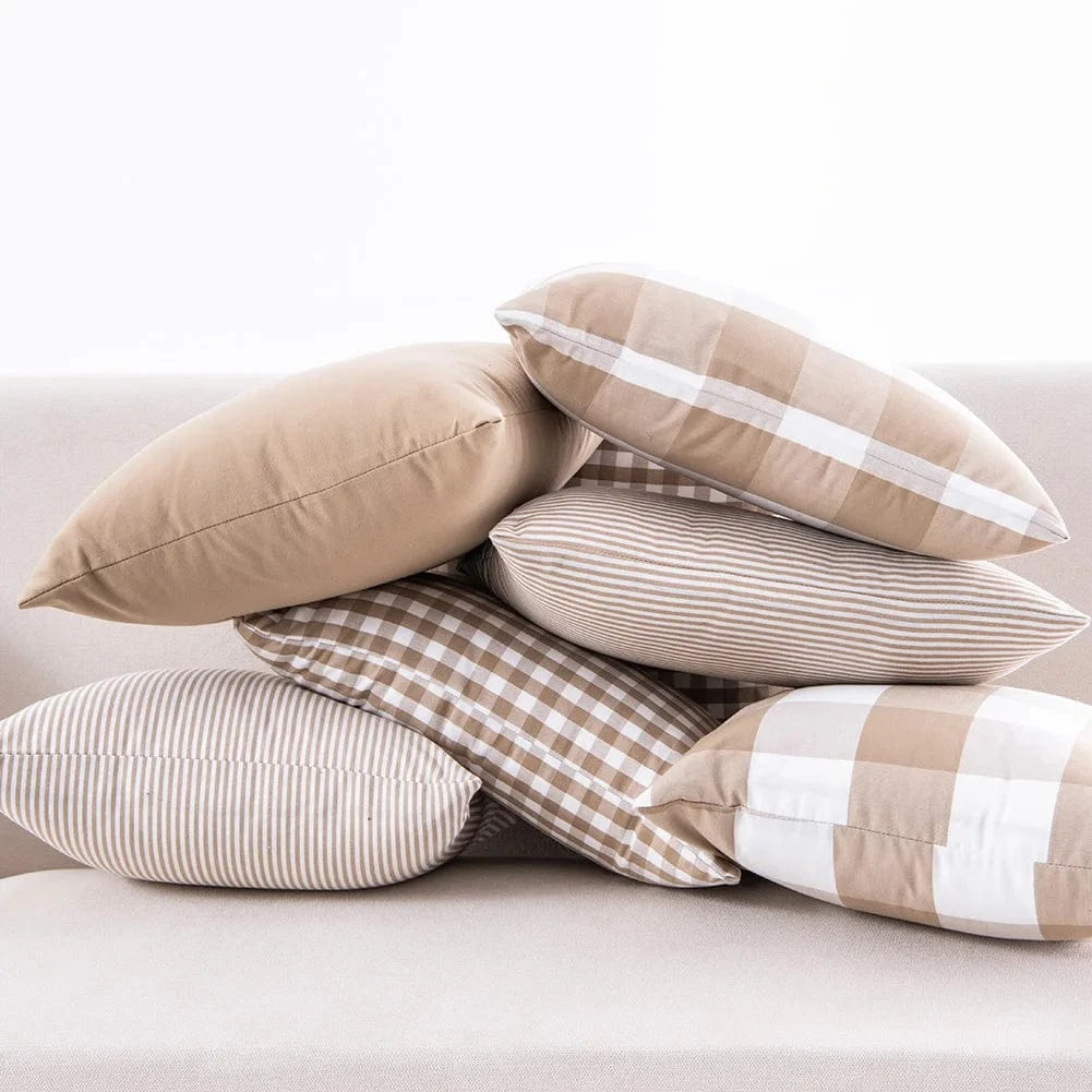 Coussins décoratifs aux motifs rayés et à carreaux, dans des tons beige, disposés sur un canapé moderne