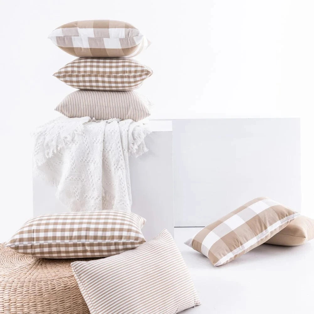 Coussins décoratifs aux motifs à carreaux et rayures, disposés sur un pouf en osier et une couverture blanche