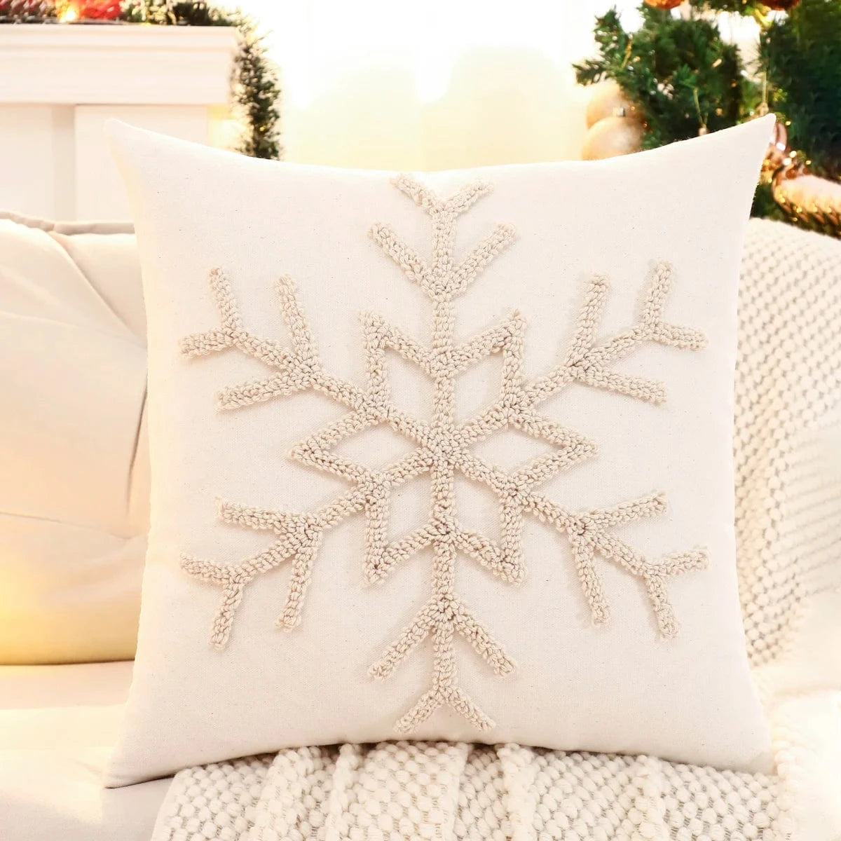 Coussin décoratif beige avec un motif de flocon de neige, posé sur un canapé cosy dans une ambiance festive