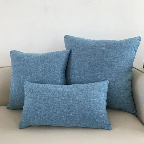 Trois coussins déco en tissu bleu clair, disposés sur un canapé beige, apportant une touche de confort et de style