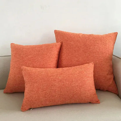 Trois coussins décoratifs en tissu orange, disposés sur un canapé beige, apportant une touche chaleureuse au salon