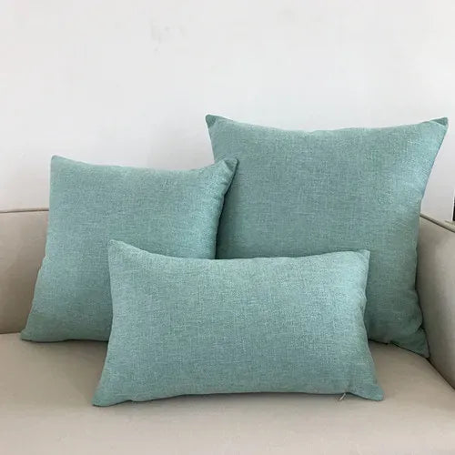 Trois coussins décoratifs en tissu vert pastel, posés sur un canapé beige, créant une ambiance apaisante
