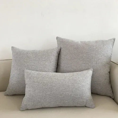 Trois coussins décoratifs en tissu gris clair sur un canapé beige, apportant une touche moderne au salon