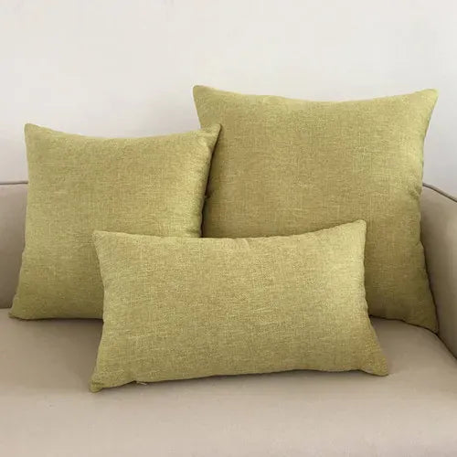 Trois coussins décoratifs de couleur vert clair en tissu texturé, posés sur un canapé beige