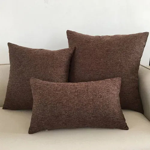Trois coussins décoratifs en tissu marron, disposés sur un canapé beige, ajoutant une touche chaleureuse au salon