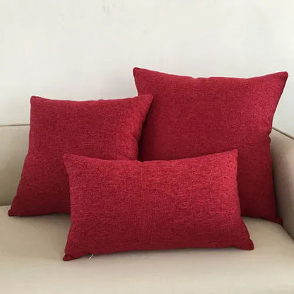 Trois coussins décoratifs rouges en tissu texturé disposés sur un canapé beige, ajoutant une touche de couleur au salon