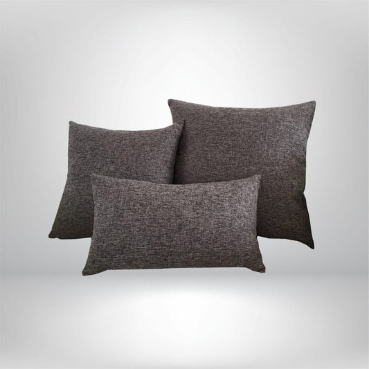Trois coussins décoratifs gris en tissu texturé, posés sur un fond neutre, parfaits pour un salon moderne