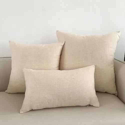 Trois coussins décoratifs beige en tissu texturé, posés sur un canapé clair dans un salon moderne