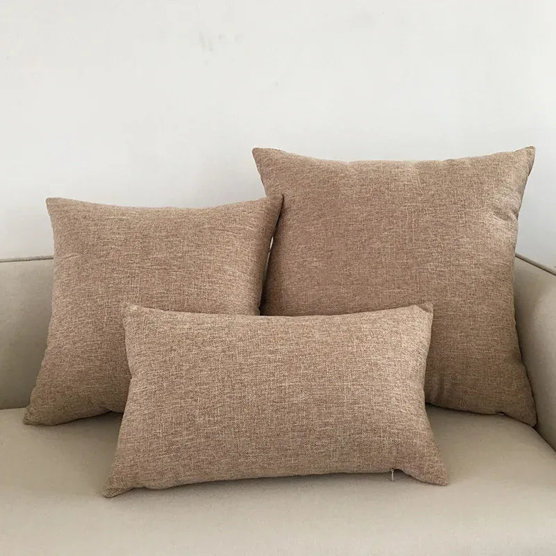 Trois coussins décoratifs en tissu beige, disposés sur un canapé clair, apportant une touche chaleureuse au salon