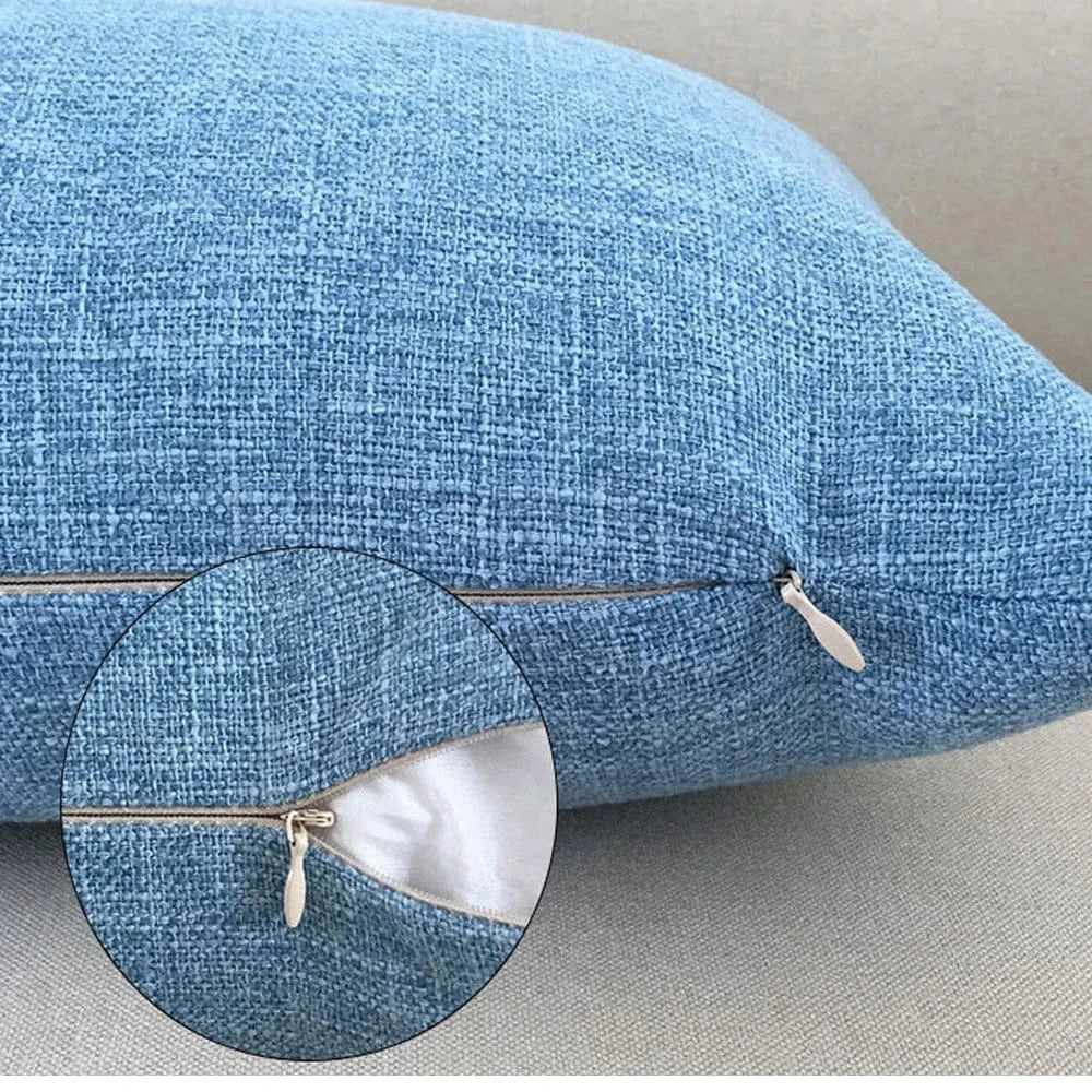 Housse de coussin bleu en tissu texturé, avec fermeture éclair, posée sur un canapé clair dans un salon moderne