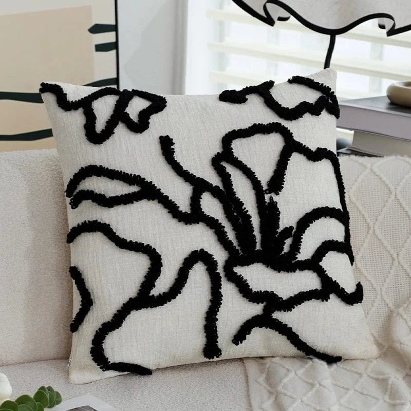 Coussin décoratif aux motifs géométriques noirs sur fond crème, posé sur un canapé moderne
